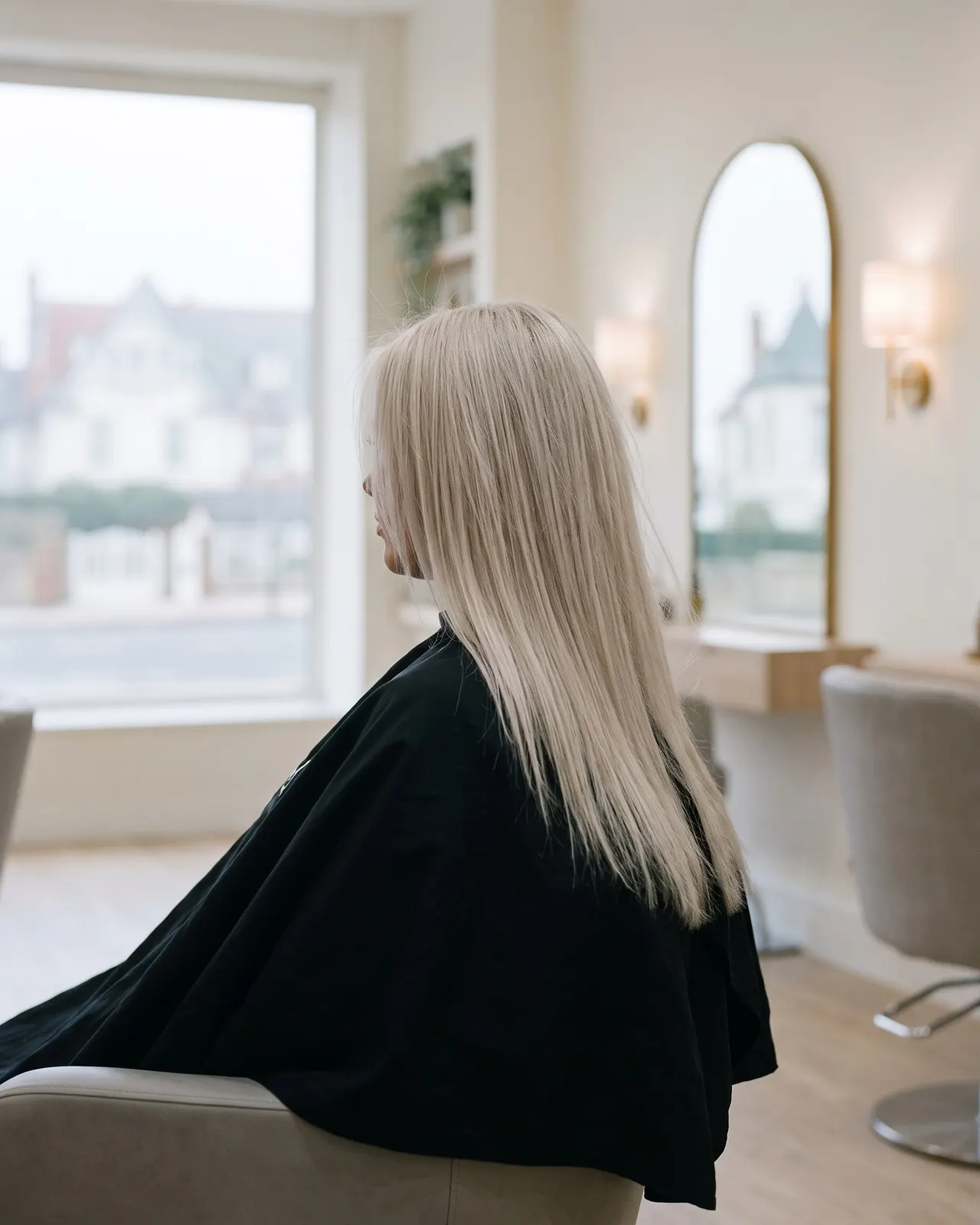 Blond polaire uniforme sur cheveux longs lisses, cliente de dos devant le miroir en arche